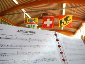 Die drei, von der Decke hängenden, Fahnen von Zimmerwald, der Schweiz und Bern. Im Vordergrund das Stück "Adventures" auf einem Notenständer.
