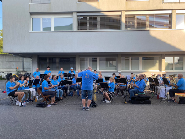 Musikgesellschaft vor einem eckigen Gebäude mit Überhang