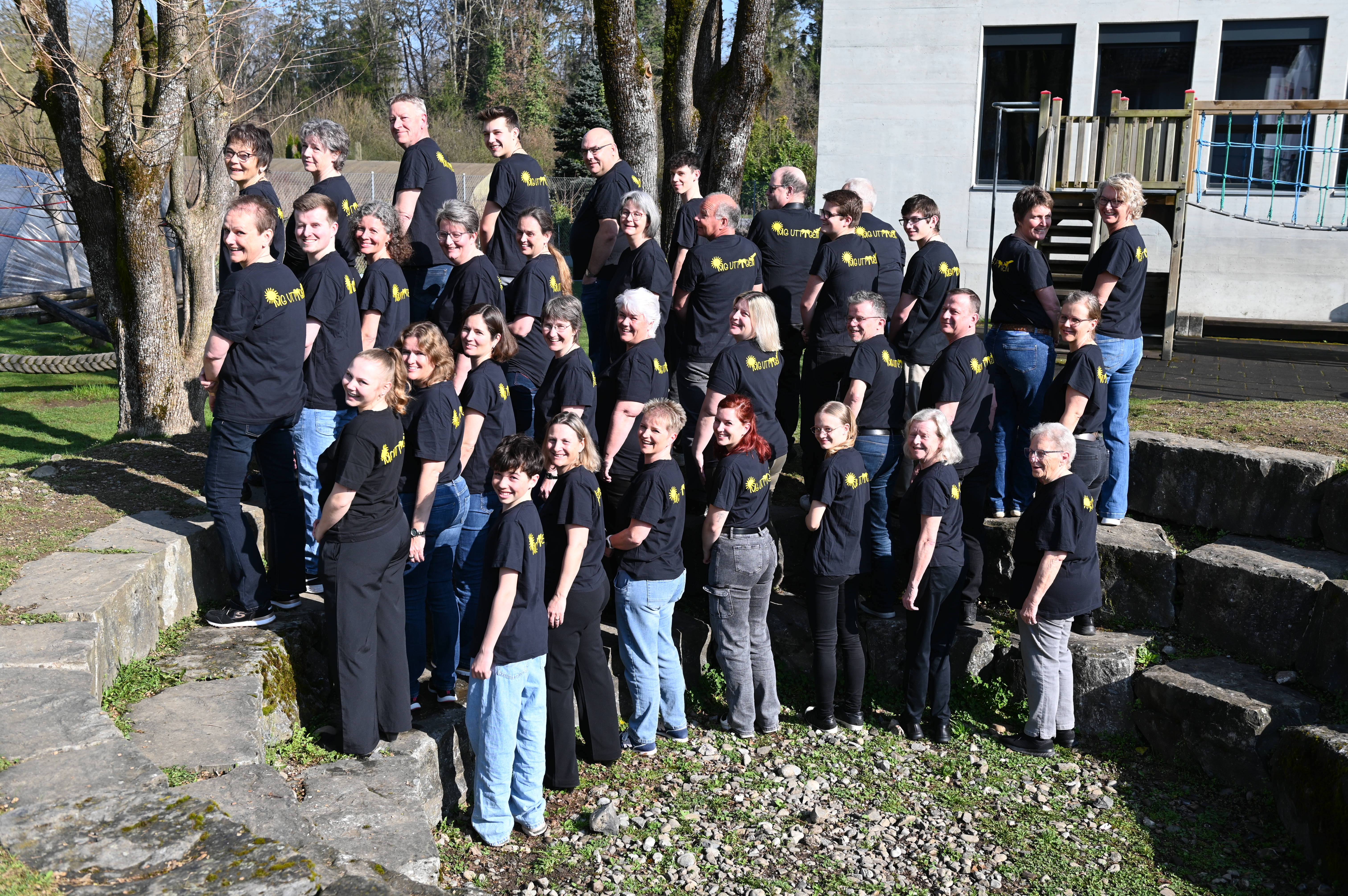 MG Uttigen mit dem Rücken zur Kamera. Die Musikanten schauen über die linke Schulter in die Kamera.