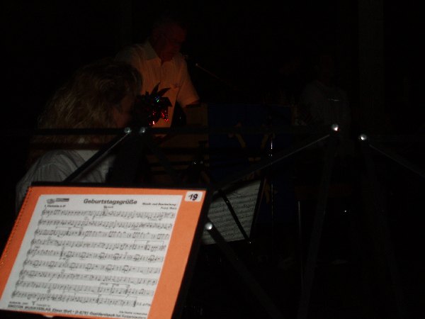 Geburtstagsgrüsse auf einem Notenständer. Im Dunklen dahinter fast nicht zu sehen: eine Querflötenspielerin.