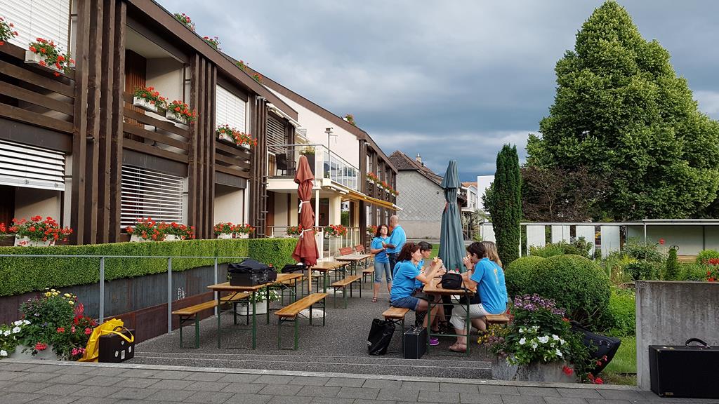 Seitenansicht des Altersheims. Davor sitzen an einem langen Tisch MGUler mit blauen T-Shirts.