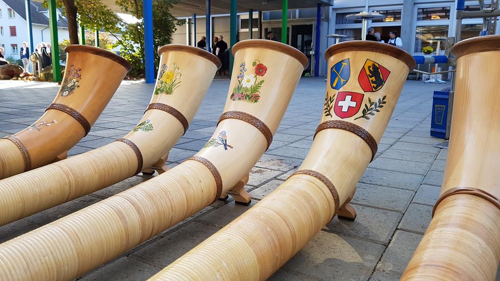 Fünf, am Boden bereit liegende, Alphörner. Jedes hat eine andere Verzierung.