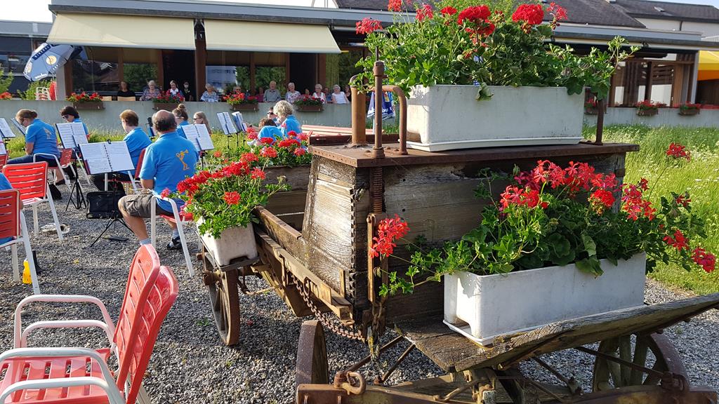 Alter Wagen, dekoriert mit Geranienkisten. Im Hintergrund die sitzende MGU.