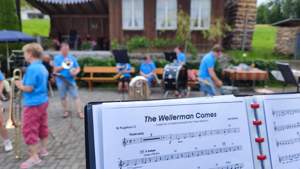 Notenbuch im Vordergrund. Musikgesellschaft im Hintergrund (unscharf)