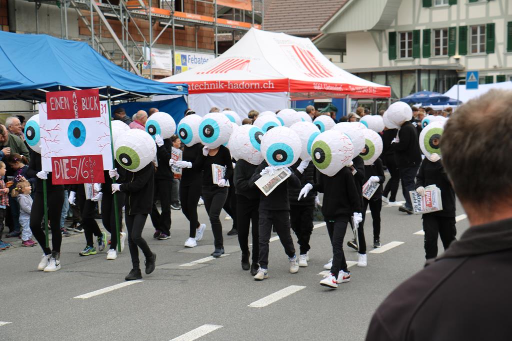 Schwarz gekleidete Schulkinder der 5. & 6. Klassen. Auf dem Kopf tragen sie ein überdimensionales Auge. Ihr Motto: Augenblick.