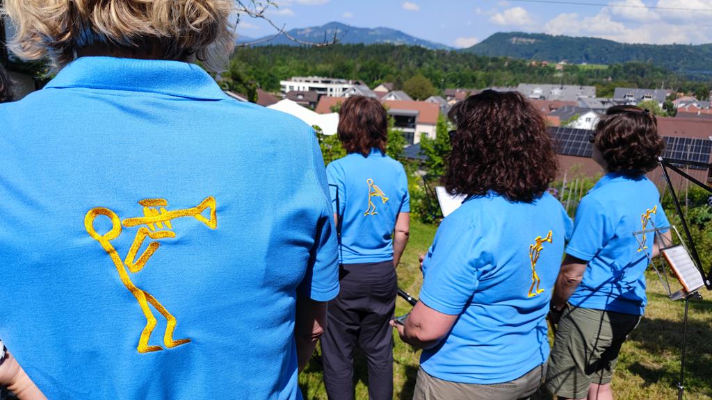 Die Musikgesellschaft Uttigen mit den blauen T-Shirts. Die, auf den Rücken, aufgestickten Logos sind erkennbar.